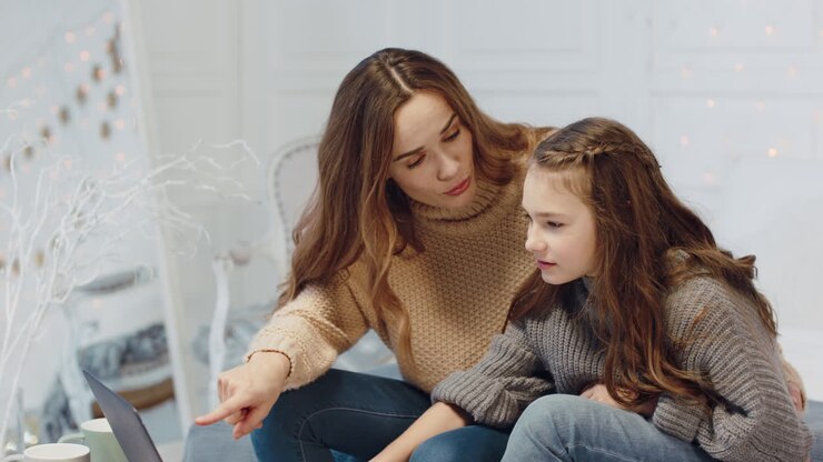 Lächelnde Mutter und Tochter sitzen vor dem Laptop in einem Luxushaus