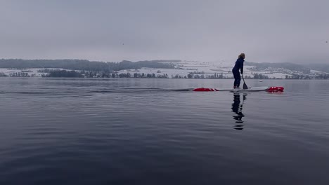 slow motion footage of a woman on a stand-up-paddleboard sup on a lake in switzerland in winter