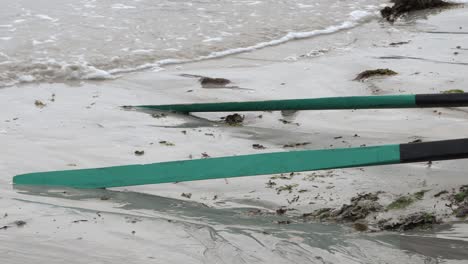vista estática de remos de currach descansando en la arena húmeda mientras las olas se acarician sobre ellos