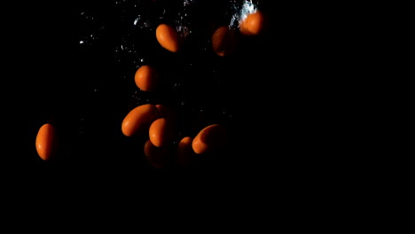 Cherry-tomatoes-dropped-into-water-on-black-background,-side-lit-slow-motion