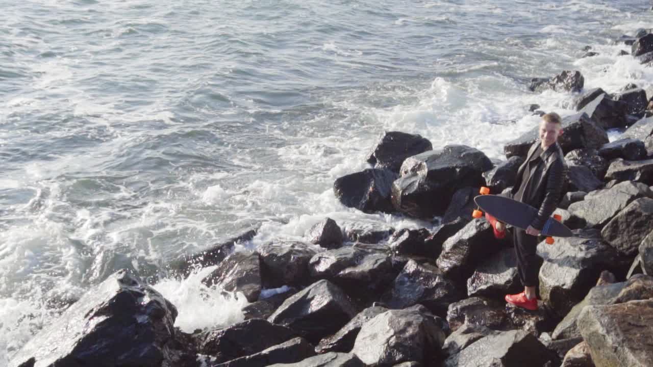 젊은 남자가 그의 롱보드와 함께 바 ⁇ 가에 서 있습니다.