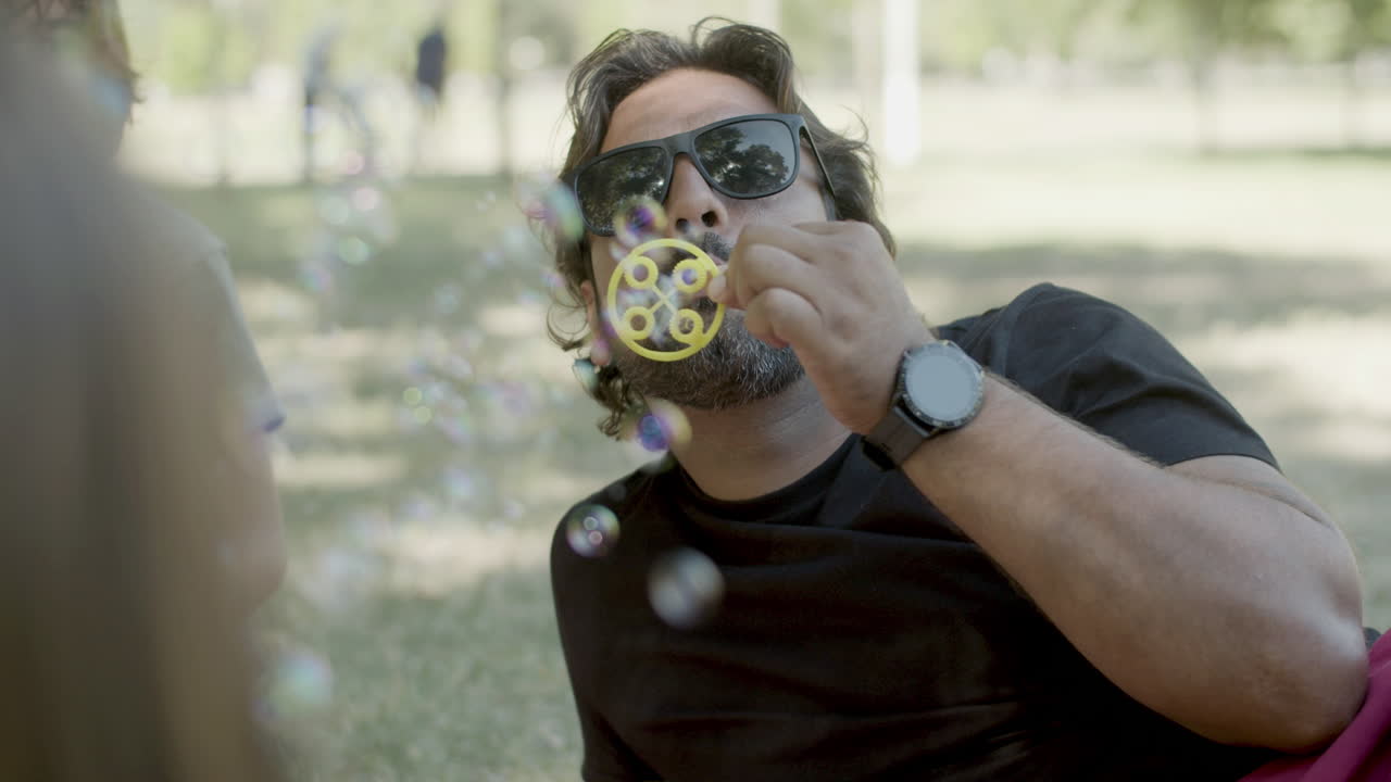 Medium shot of single bearded father blowing soap bubbles