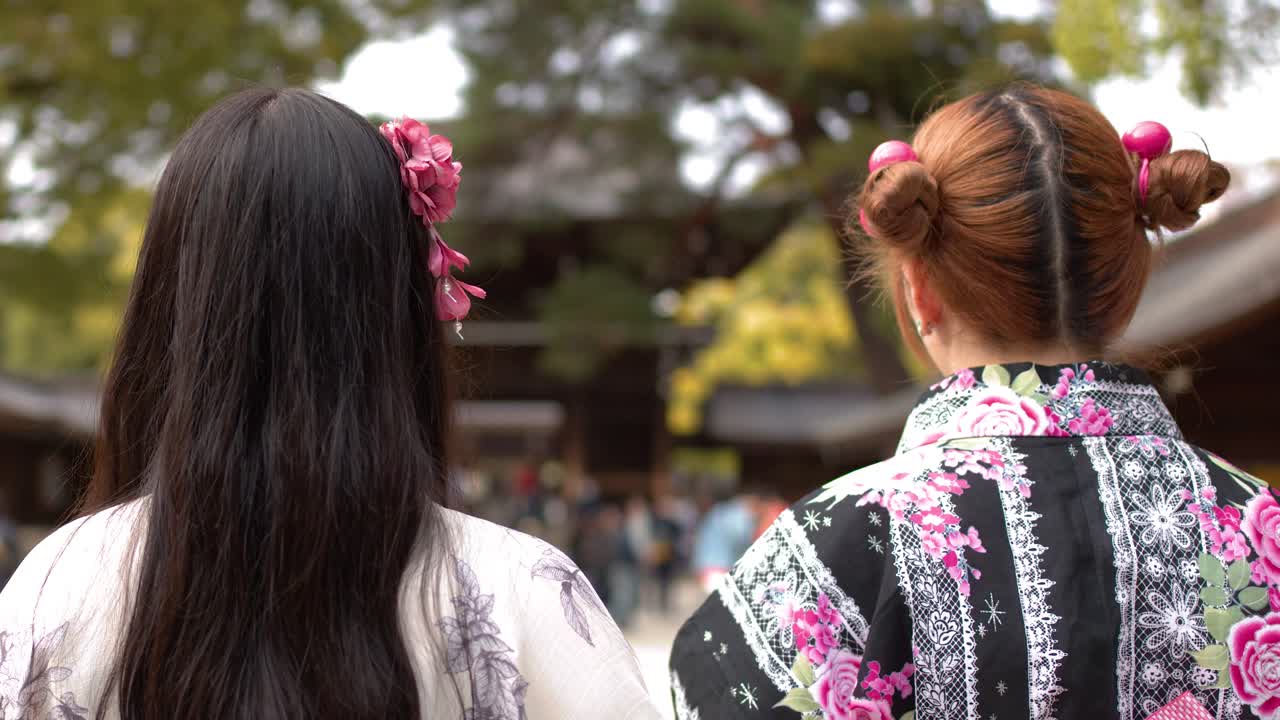 花柄の着物を着た二人の女性が、日本の神社の本殿に向かって丁寧に頭を下げる。