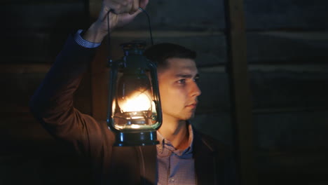 the frightened man in a suit standing in a dark room covers himself around a kerosene lamp