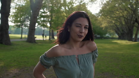 retrato en cámara lenta de una hermosa joven hispana latina mirando a la cámara, parpadeando y coqueteando, con un hermoso parque británico en el fondo