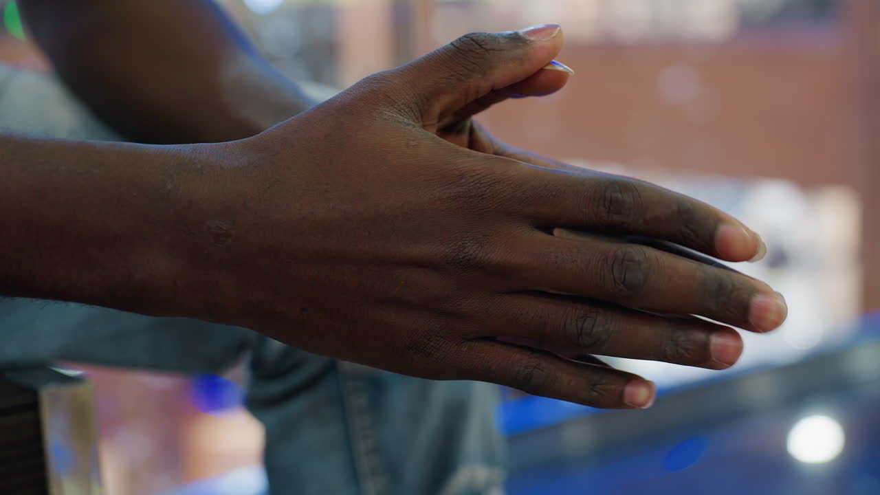 Side hand view of dark skin person tapping hand thoughtfully in indoor setting showing detailed close up of natural skin texture and subtle gesture while seated in casual outfit