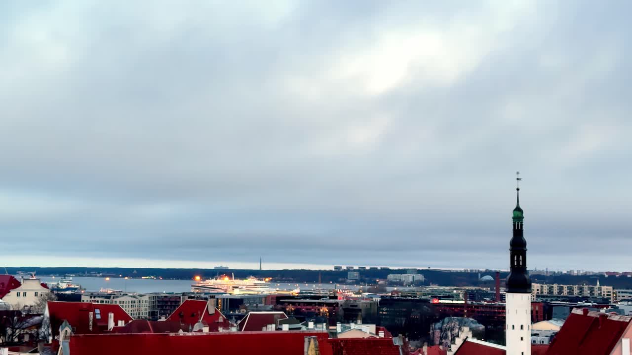 Tallinn, Estonia: veduta paesaggistica cinematografica dall'alto dei tetti rossi della Città Vecchia medievale e della baia del porto sotto un cielo invernale cupo e coperto, con una grande nave da crociera bianca ormeggiata durante il crepuscolo dell'ora blu.