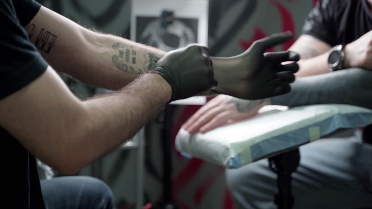 Unrecognizable male tattooist putting on gloves before work in salon