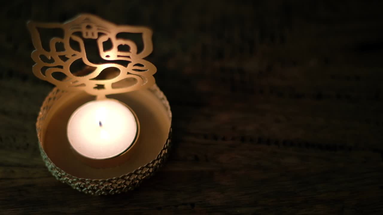 Closeup of a man's hand lighting a wax tea candle in front of Lord Ganesha golden cutout during Diwali, festival oof lights, worship celebrations with a lighter in dark to show the light.