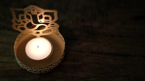 closeup of a man's hand lighting a wax tea candle in front of lord ganesha golden cutout during diwali, festival oof lights, worship celebrations with a lighter in dark to show the light.