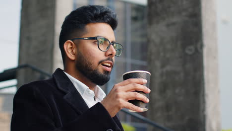 Happy-Indian-business-man-enjoying-morning-coffee-hot-drink-relaxing-taking-a-break-in-downtown-city