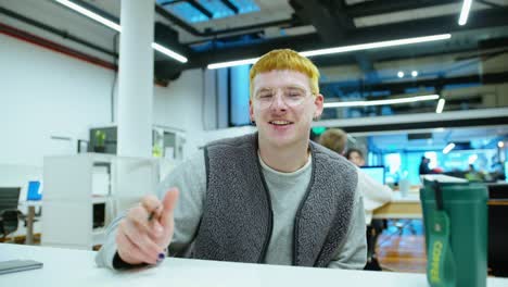 young gen z man smiling and shaking at camera during working day in office