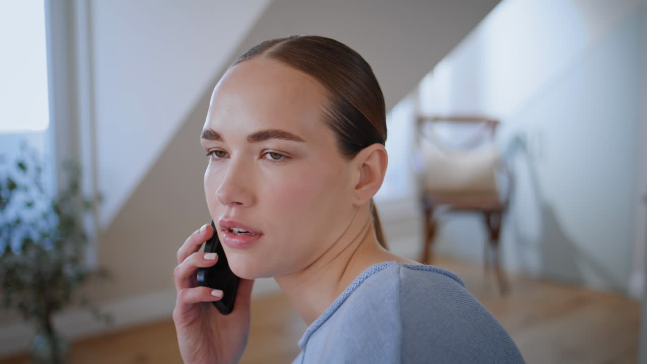 Serious woman calling mobile phone at home closeup. Calm attractive girl talking