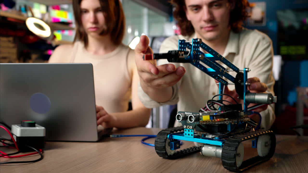 Two young happy engineers fixing a mechanical robot car in the workshop, computer programming