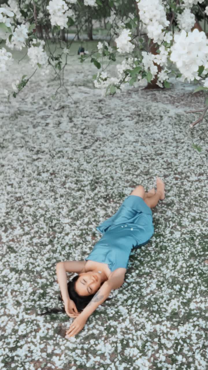 Woman in a blue satin dress relaxing in a park covered in white flowers