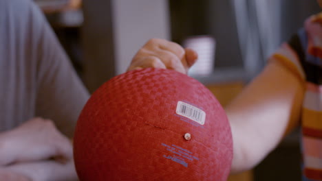 middle-aged male caregiver gently assists the hemiplegic right hand ball therapy of a senior female stroke survivor, seated by glass top kitchen table at home. back, and forth hand motion. 24fps.