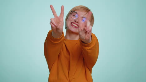 Young woman in glasses showing victory sign hoping for success and win doing peace gesture smiling