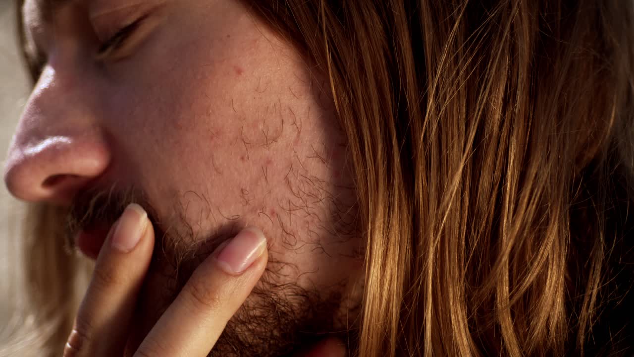 The Woman Gently Runs her Fingers Over the Man's Lips as They Sit Together on the Beach in The Netherlands - Close Up