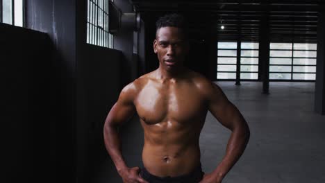 hombre afroamericano sin camisa flexionando sus músculos en un edificio urbano vacío
