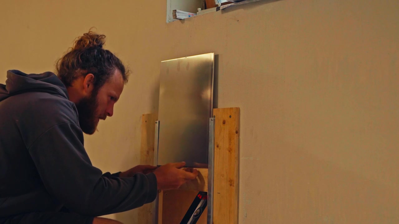 Un uomo sta regolando una copertura metallica scorrevole su una piccola apertura nel muro - Primo piano