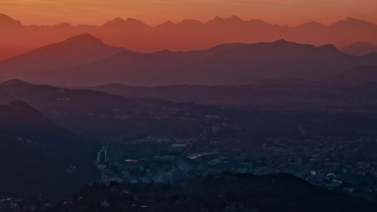 impresionante color de puesta de sol atrapado en la niebla y la neblina sobre las montañas detrás de la ciudad en el valle de abajo