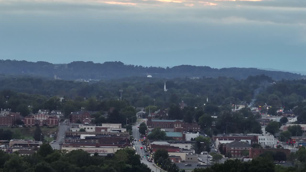 Cloudy dusk scene in small American town with traffic on Main Street. Aerial tilt up wide shot. Lighting streets and red brick historic buildings in downtown. Zoom shot