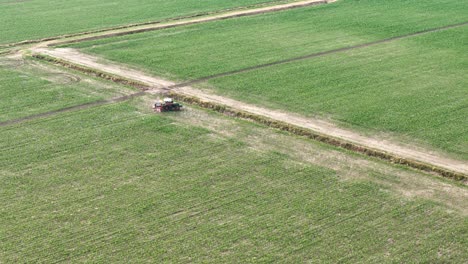 aerial of tractor applying chemical pesticides on a vast monoculture maize field, highlighting environmental and health concerns linked to gmo crops and intensive industrial agriculture practices