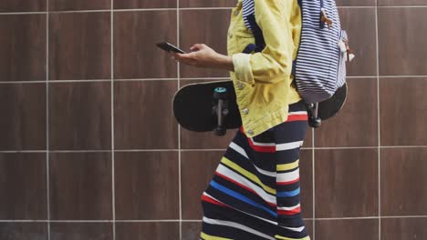 mixed race woman walking on street holding her skateboard and her phone