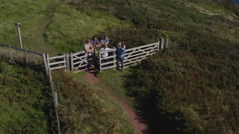 drone shot of friends hiking along cliffs on coastal path resting by gate and waving at camera