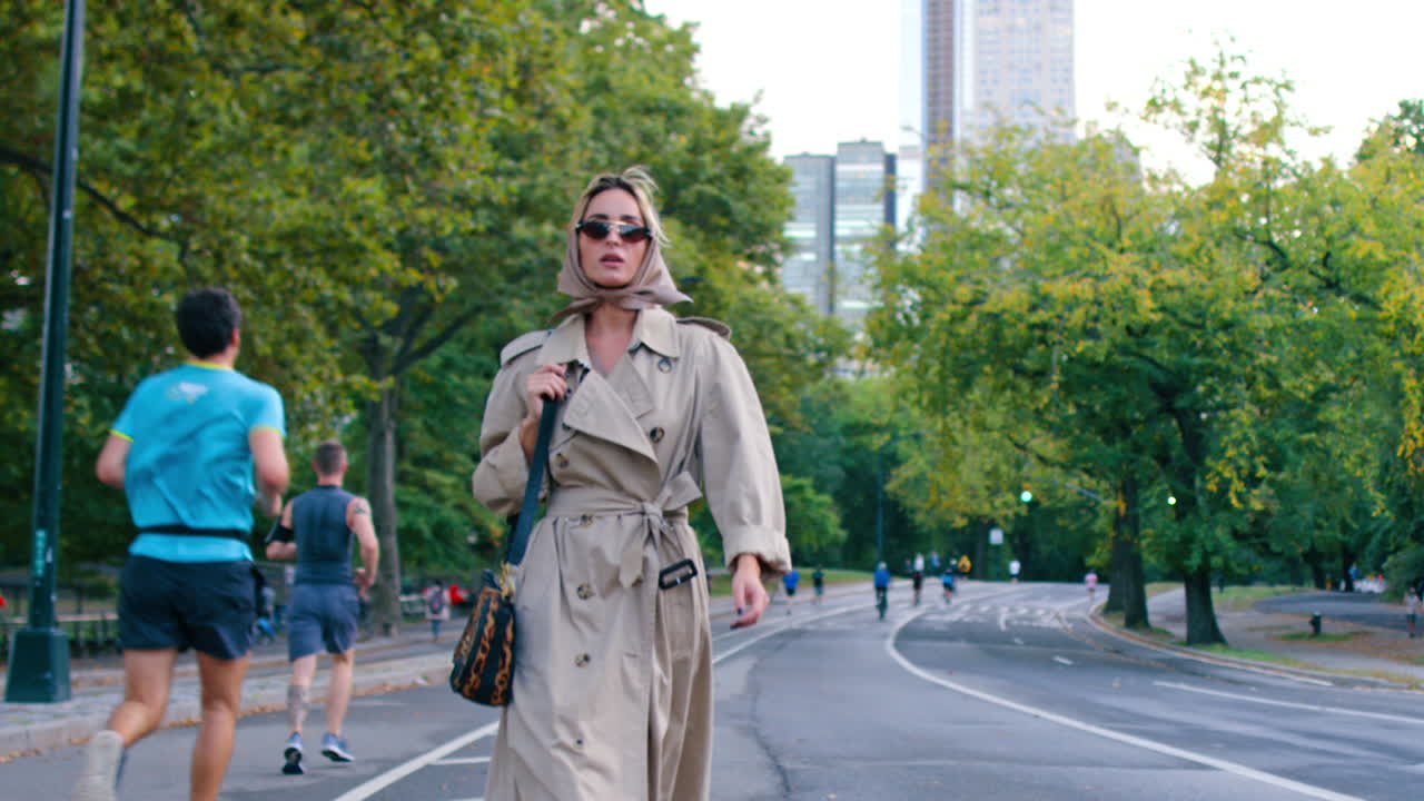 New York, USA, 2 aprile 2026: Donna in trench e foulard che cammina nel parco. Figura intera di una donna in trench beige e foulard di seta che cammina su una strada a Central Park, New York.