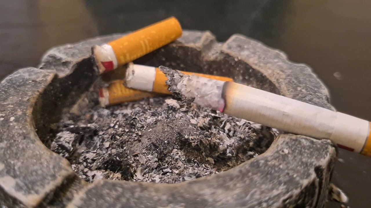 Primer plano de cigarrillo en cenicero, tabaco encendido y humo