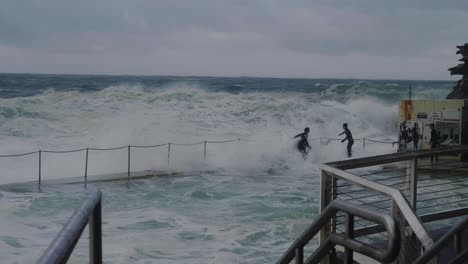 enormes olas rompiendo en la piscina en la playa de bronte con personas que corren el riesgo - tormenta peligrosa en sydney, nsw, australia - plano general