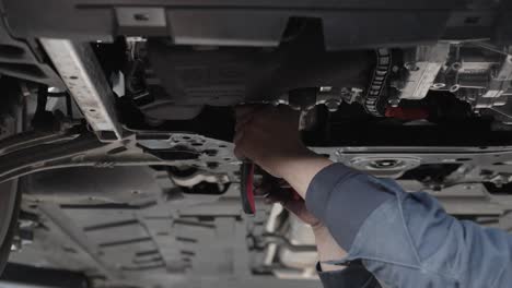 A-mechanic-under-a-car-uses-pliers