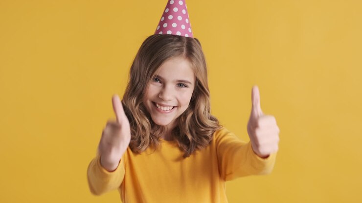 Teenage Caucasian girl with thumbs up wearing a party hat.