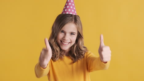 una adolescente caucásica con los pulgares hacia arriba con un sombrero de fiesta.