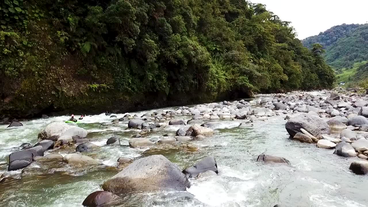 Tre kayaker gareggiano lungo un fiume pieno di sassi accanto a una scogliera della foresta amazzonica in Ecuador.