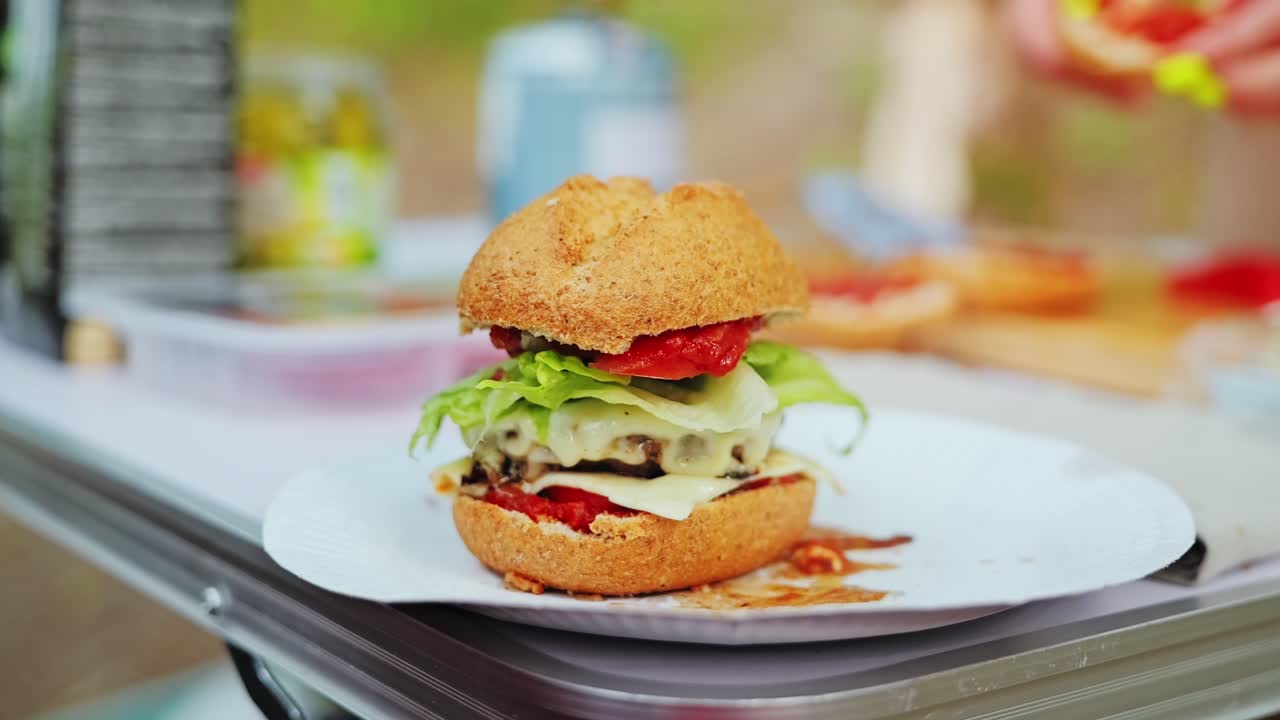 Gourmet cheeseburger stacked with layers on paper plate in forest campsite