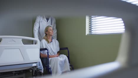 médico masculino diverso transportando a una paciente sentada en silla de ruedas en una habitación de hospital