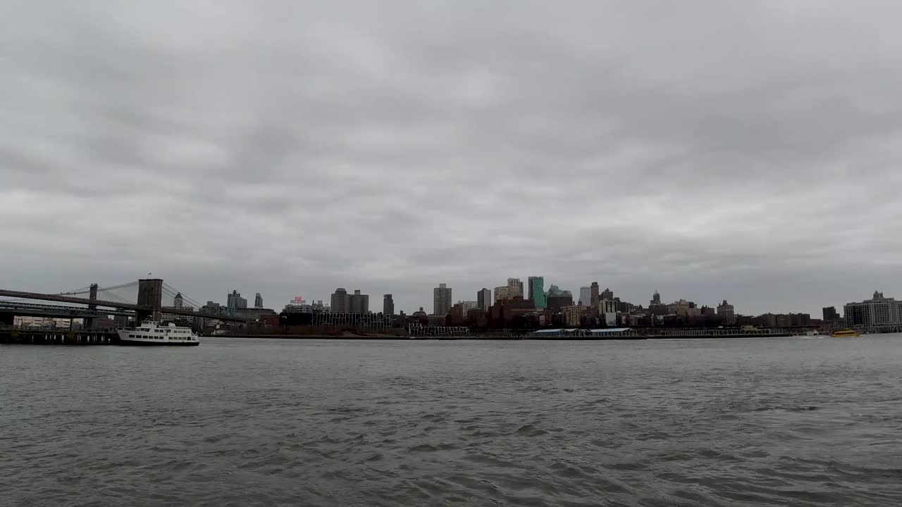 un lapso de tiempo sobre el río este del horizonte industrial de brooklyn desde manhattan mientras los barcos pasan en un día nublado