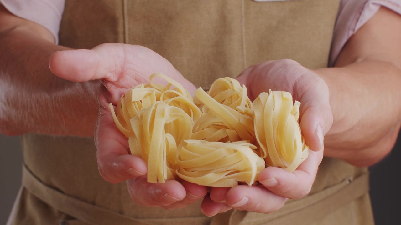 Primo piano di mani che tengono tagliatelle crude