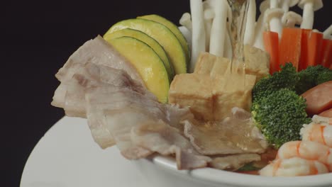 close up of pouring soup in a bowl of shabu ingredients spinning around on white table in the black background kitchen