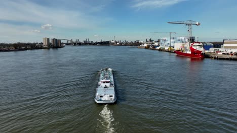 cargo boat transporting goods down canal, rotterdam, aerial medium shot following boat