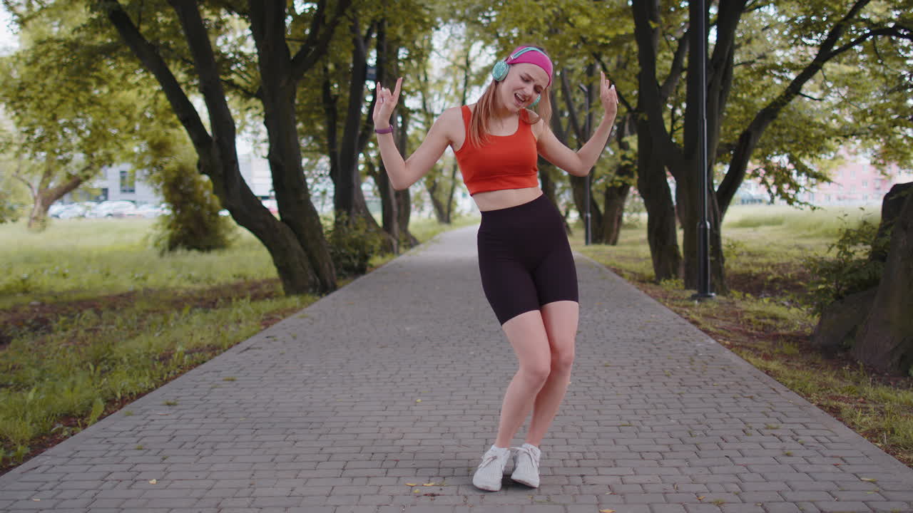 corredora deportiva chica bonita entrenamiento ejercicio escuchar música en auriculares bailar divirtiéndose en el parque