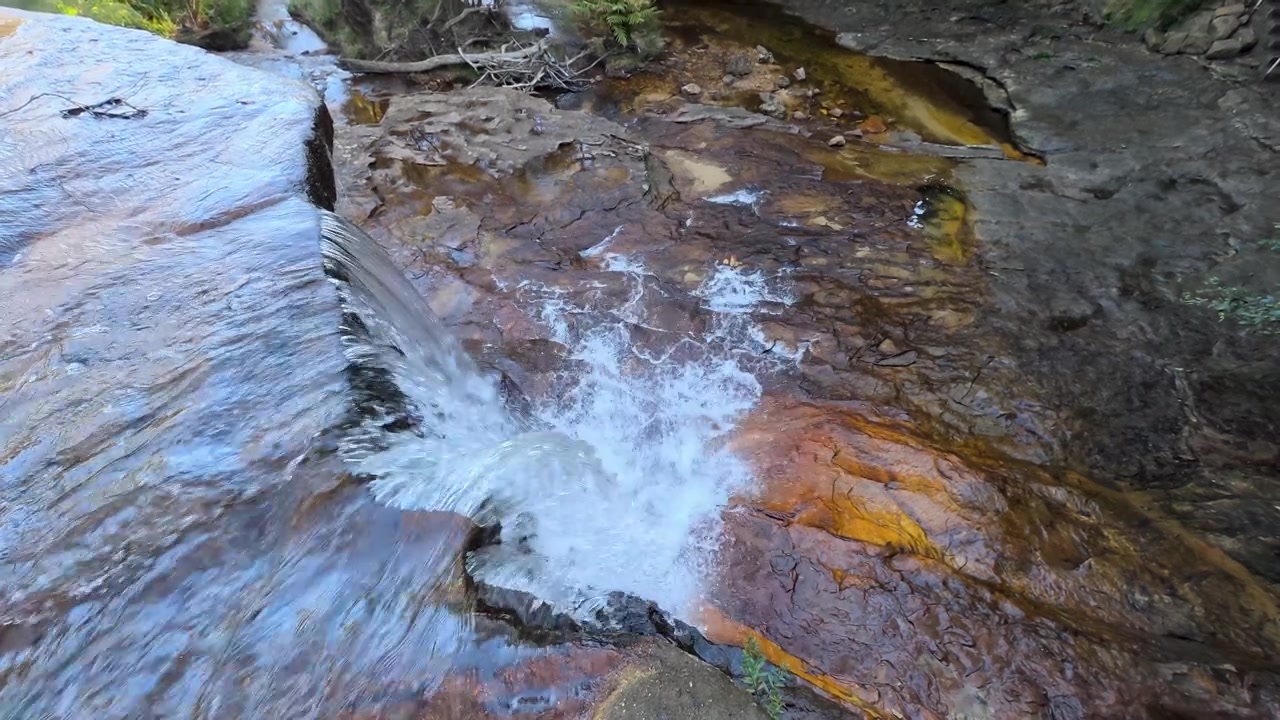 Ripresa dall'alto di acqua che scorre su rocce di arenaria nel Parco Nazionale delle Blue Mountains, Australia.