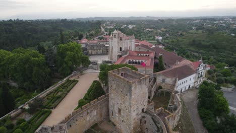 Drone-view-of-Convent-of-Christ-in-Tomar,-Portugal,-surrounded-by-lush-greenery