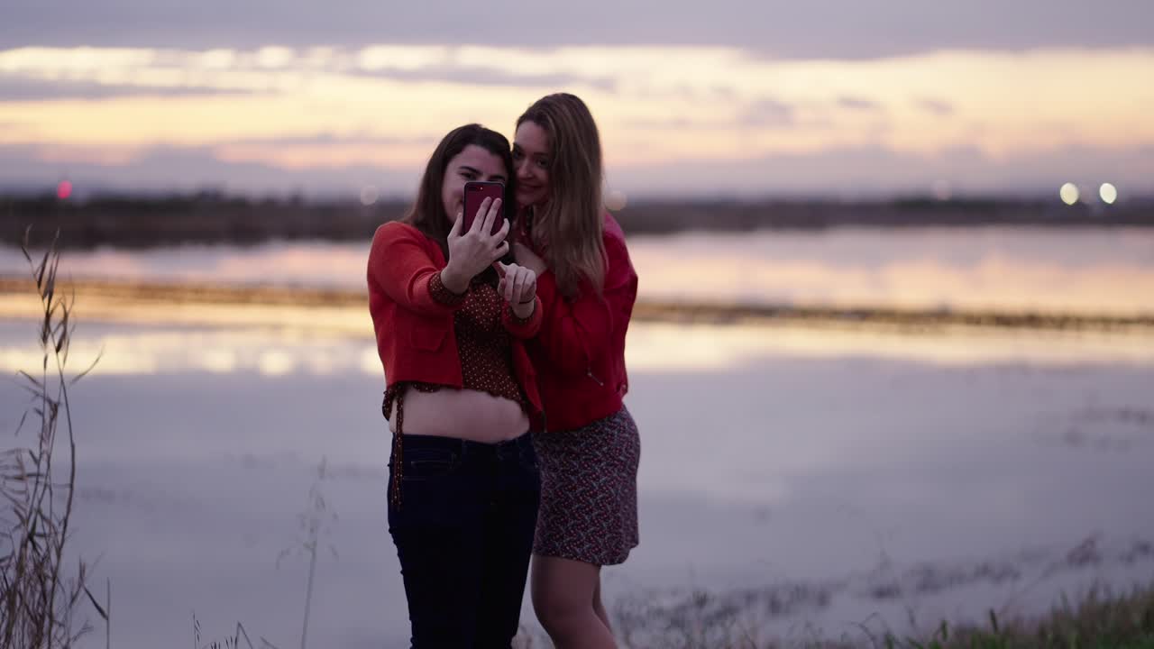 Due amici che si scattano un selfie al tramonto in riva al lago