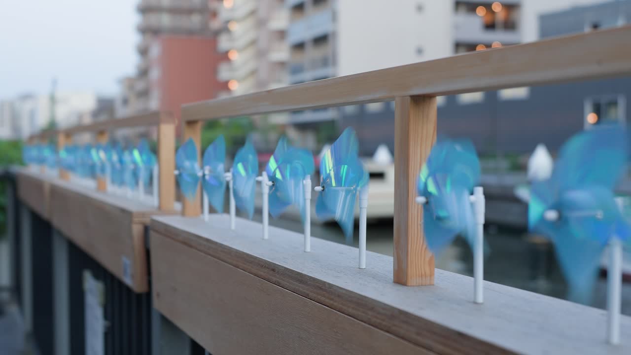 A close-up shot capturing vibrant blue pinwheels rapidly spinning in a gentle breeze, adorning the promenade railing at Tokyo Mizumachi along the Kita-jūkken-gawa River