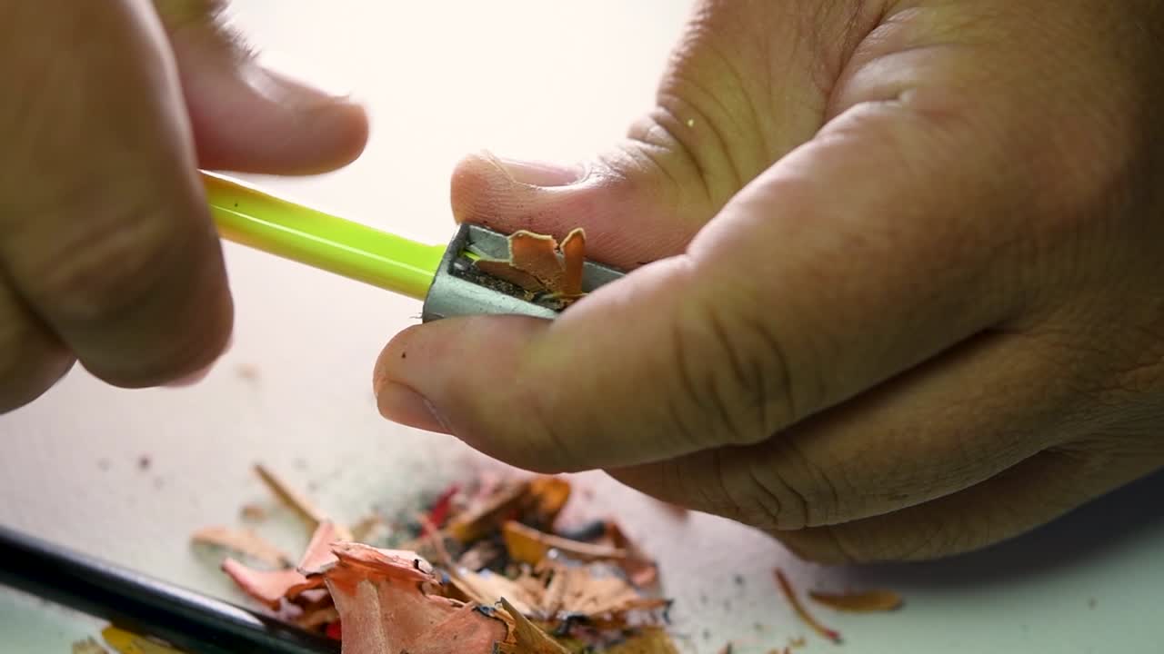 imágenes de manos afilando lentamente un lápiz y algunos lápices de colores con un sacapuntas de cuña
