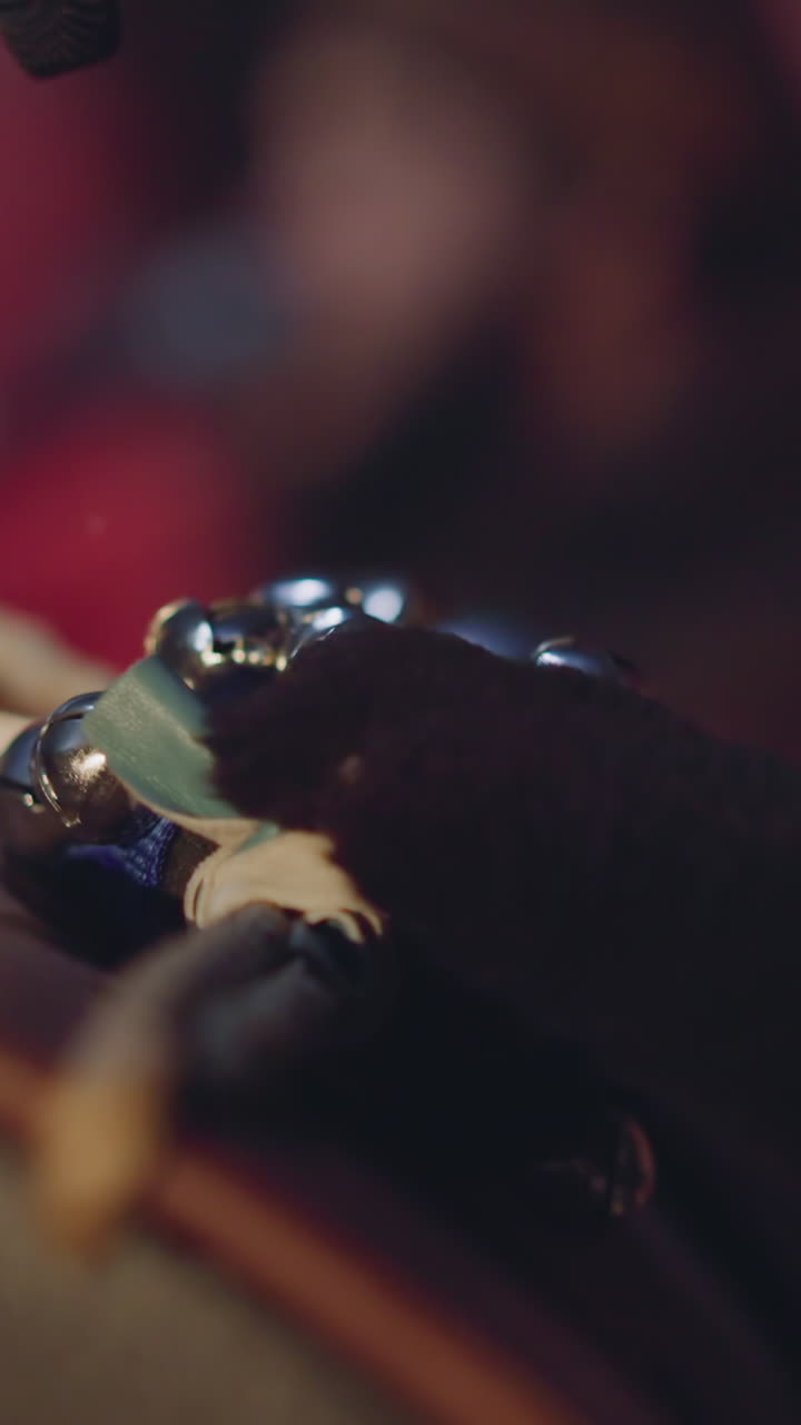 Musician taps drums with small metal bells playing folk music macro view slow motion. Drummer plays old Altai instruments at darkness. Rhythm and sound