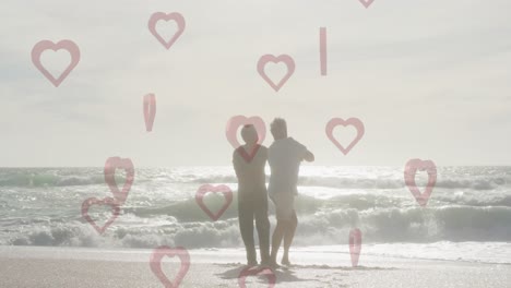 animation of red hearts over couple in love dancing on beach